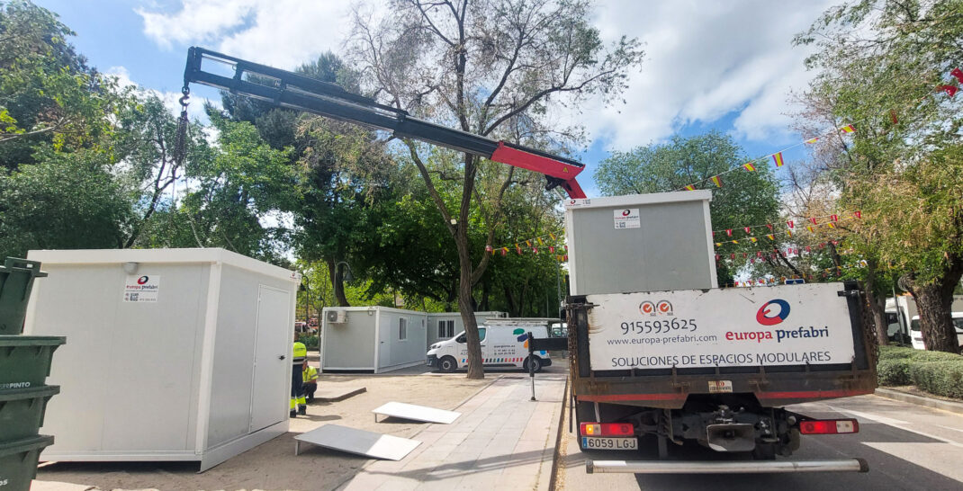 Vista frontal de dos módulos prefabricados tipo camerino instalados por Europa Prefabri para el Ayuntamiento de Pinto, con acceso independiente y acabados en blanco. En el entorno se aprecia una zona urbana destinada a actividades culturales.